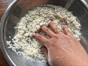 A person washing rice in a metal bowl with water