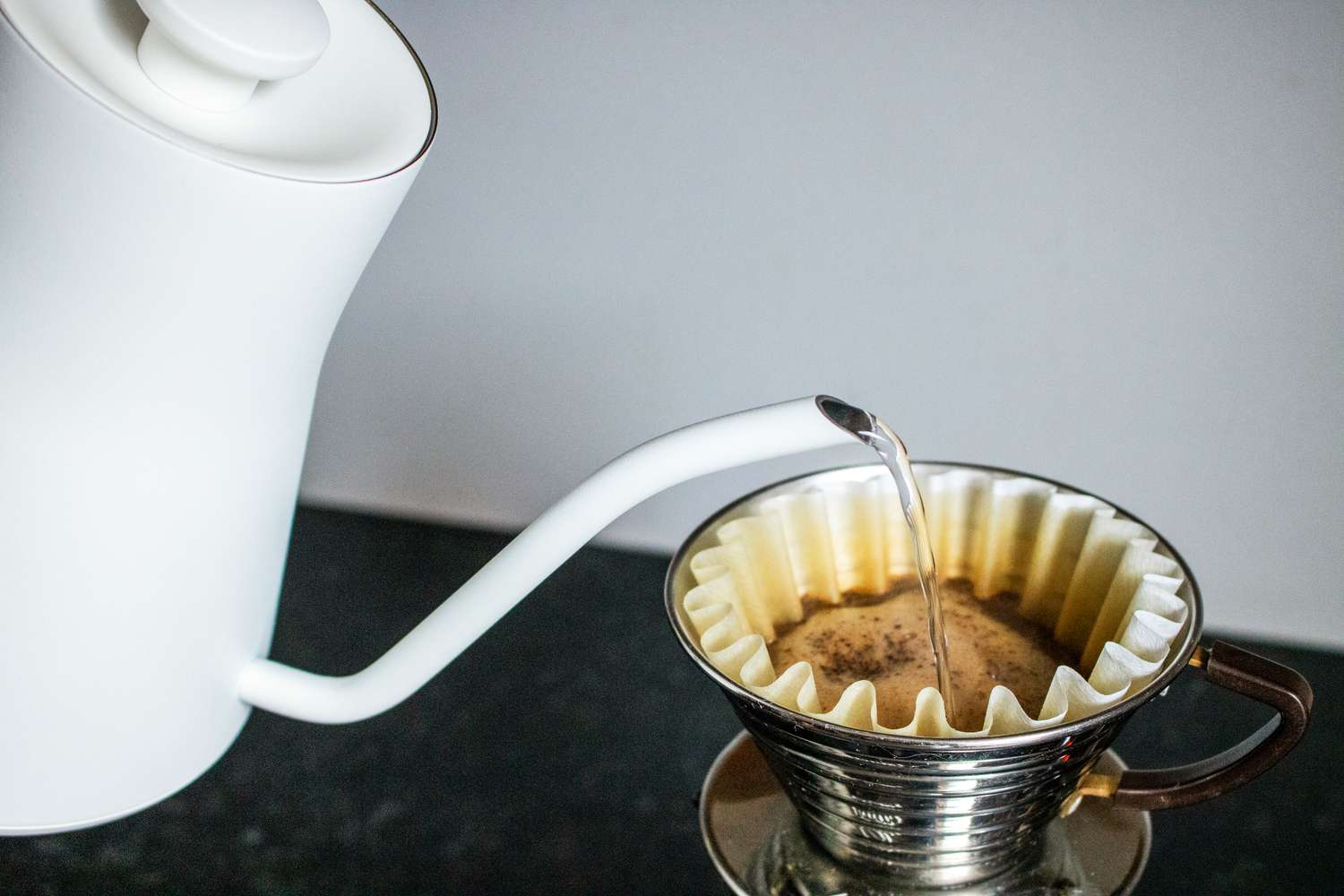 Water being poured from a white gooseneck kettle into a pourover coffee maker