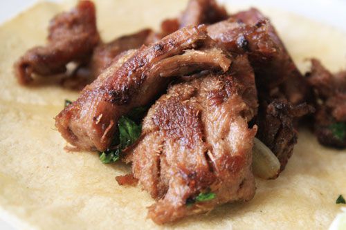 Close-up of crispy, well-browned pieces of tongue on top of a corn tortilla, a little cilantro and salsa poking out from underneath. 