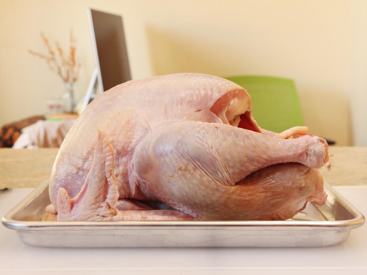 Raw, whole turkey placed on a rimmed baking sheet.