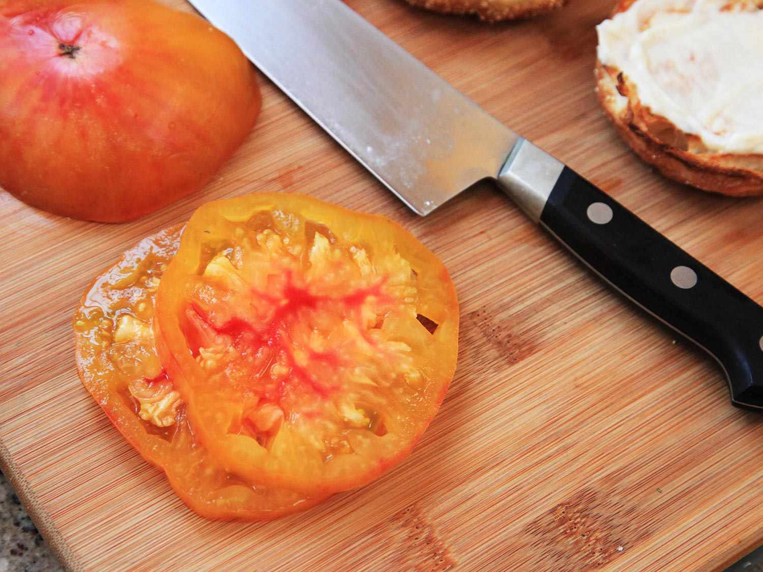 Thin slices of tomato on a wooden board next to a knife