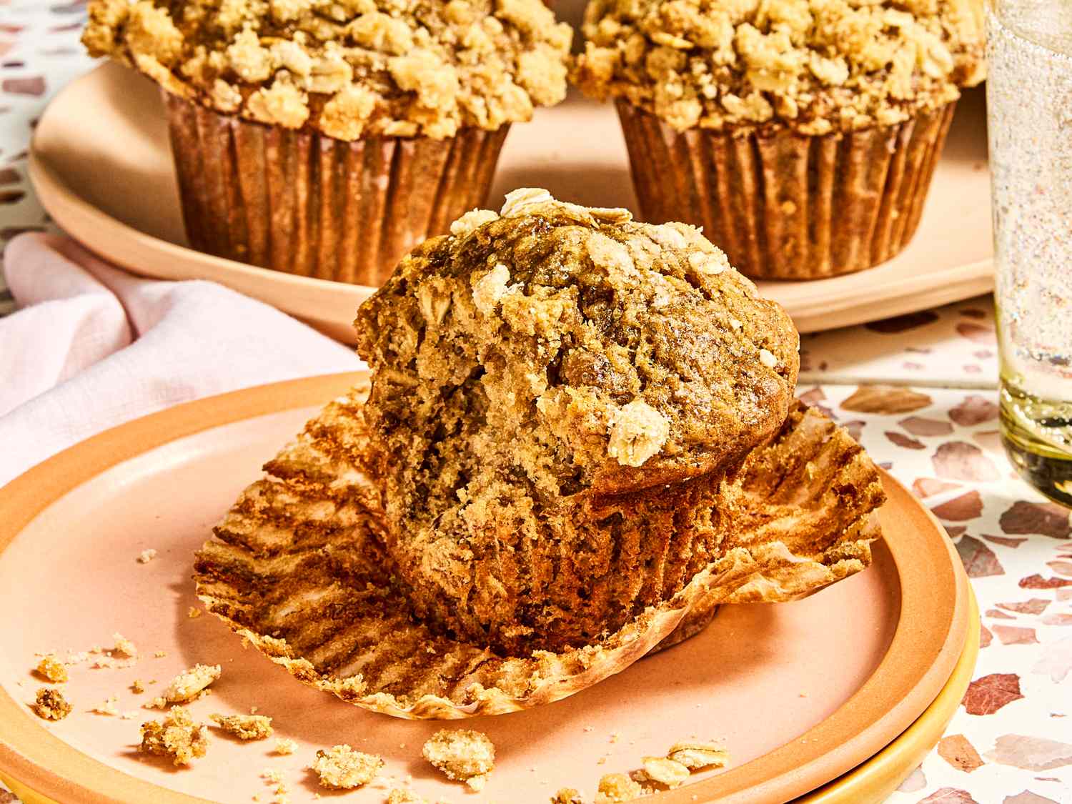 Banana oatmeal muffin unwrapped on a plate with more muffins in the background