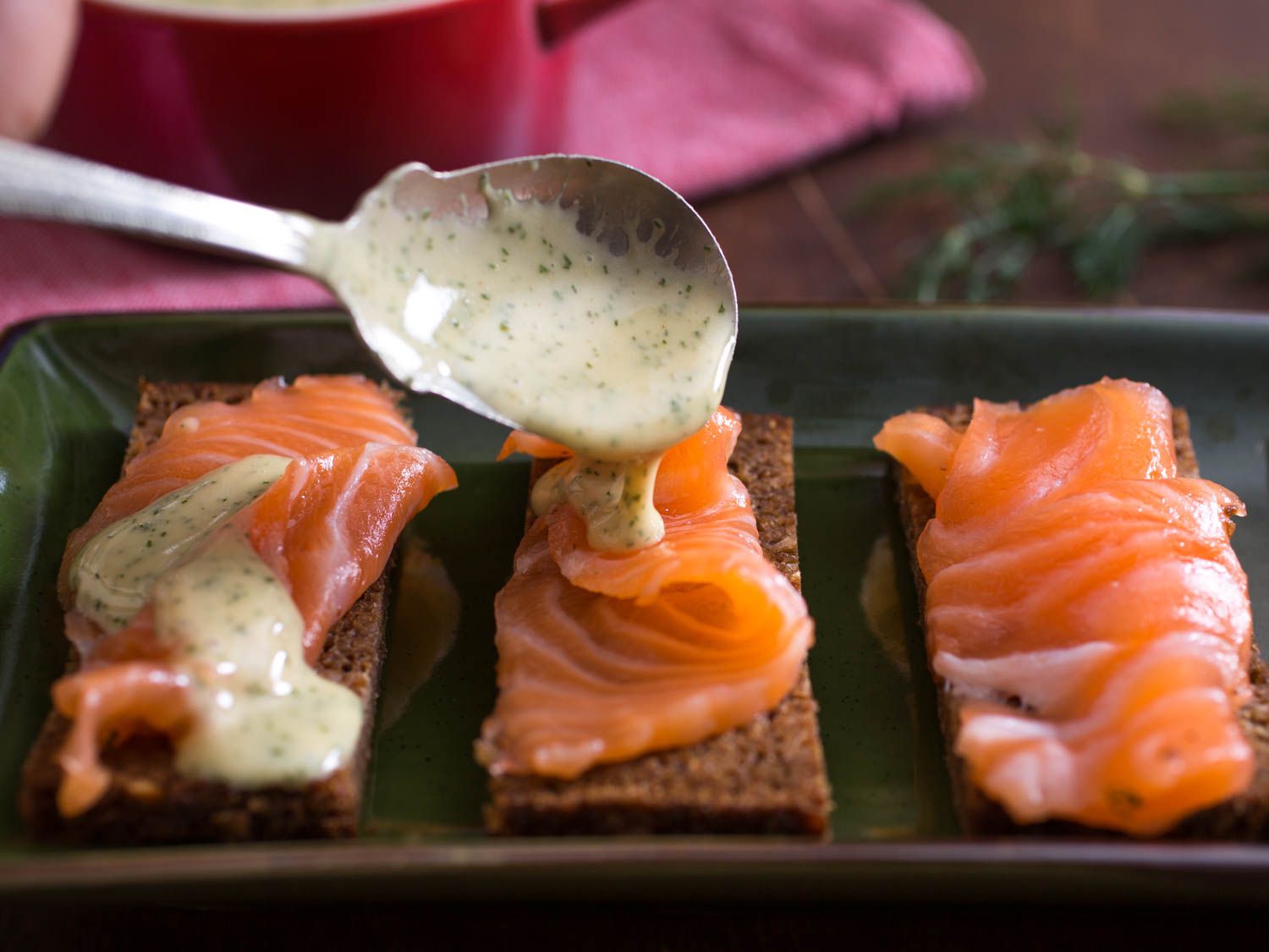 Drizzling mustard sauce over gravlax on pumpernickel bread.