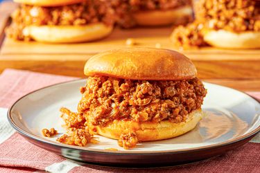 A sloppy joe served on a plate with more sandwiches in the background