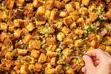 Hand adjusting pieces of bread stuffing mixed with herbs and vegetables