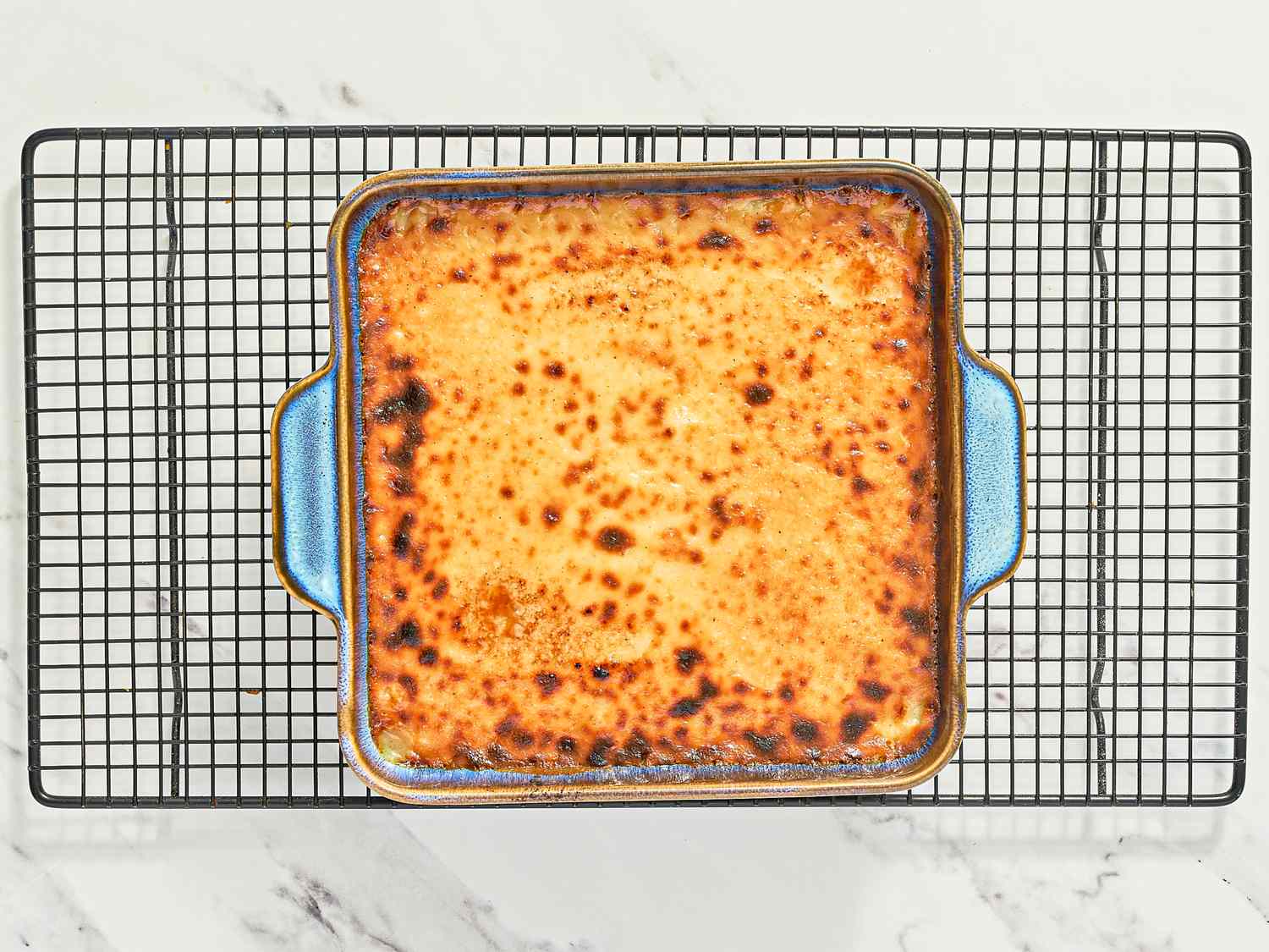 A baked dish in a square pan cooling on a wire rack