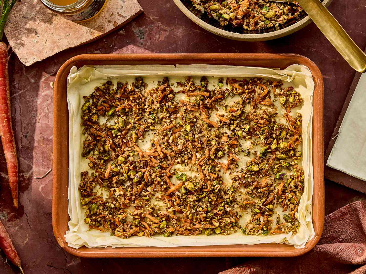 A baking dish filled with carrot cake baklava topped with nuts, placed on a table with preparation materials