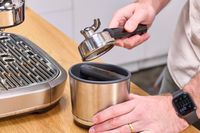 A person removes espresso grounds from the Breville The Oracle Dual Boiler Espresso Machine portafilter