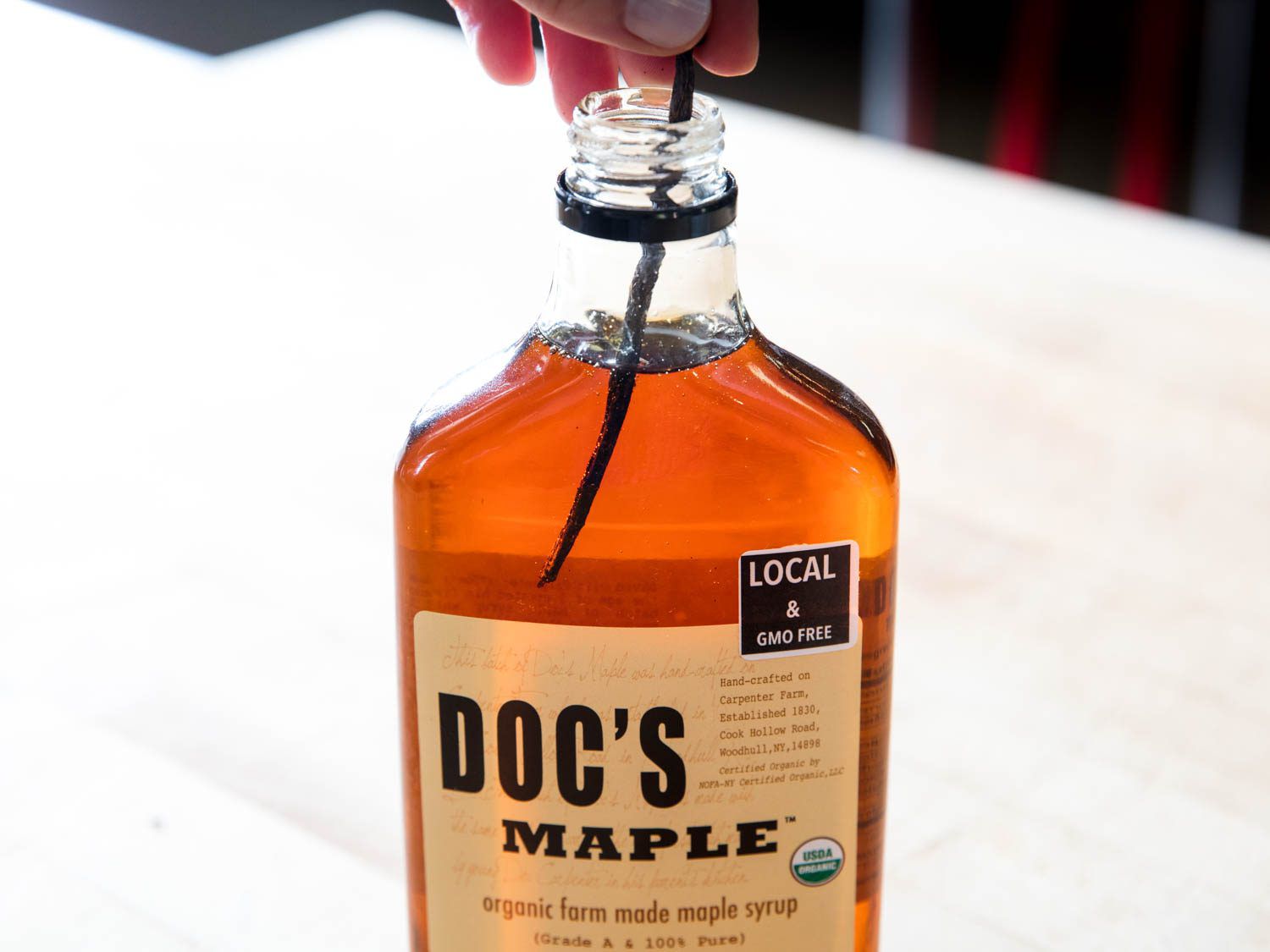 Adding vanilla bean pod to a bottle of maple syrup.