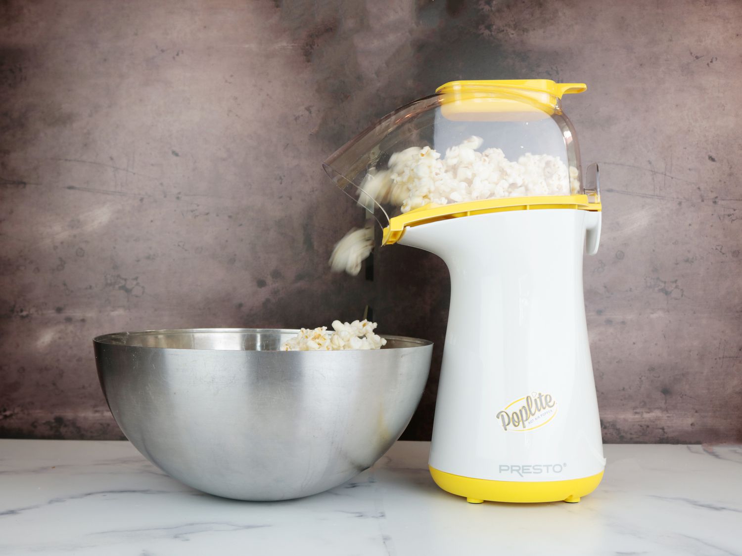 an air popper popping popcorn into a stainless steel bowl