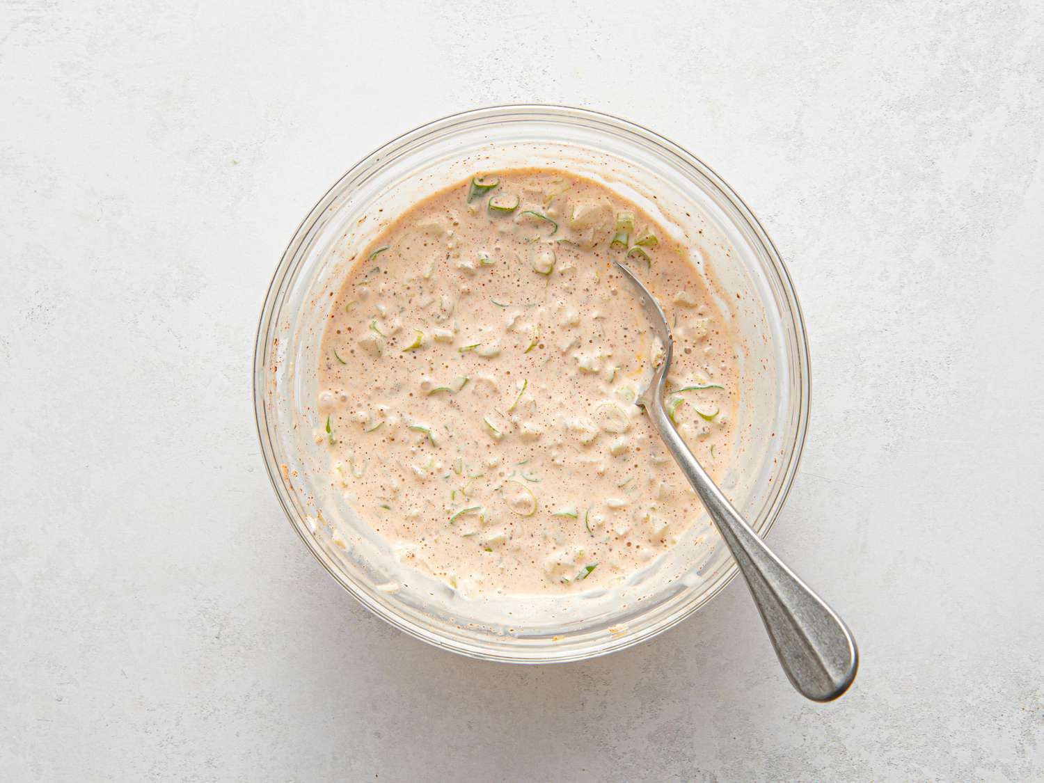 Mayonnaise, celery, scallions, lemon juice, vinegar, paprika, hot sauce, and celery seeds mixed together inside a small bowl.