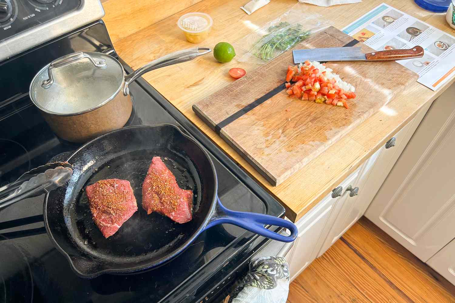 steaks searing next to a wooden cutting board with chopped tomato 