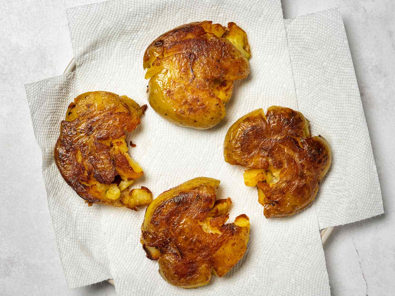 Four crispy smashed potatoes resting on multiple sheets of paper towels to drain off any excess oil.