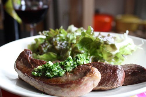 Pan seared beef heart with a green herb sauce and salad on a white ceramic plate.