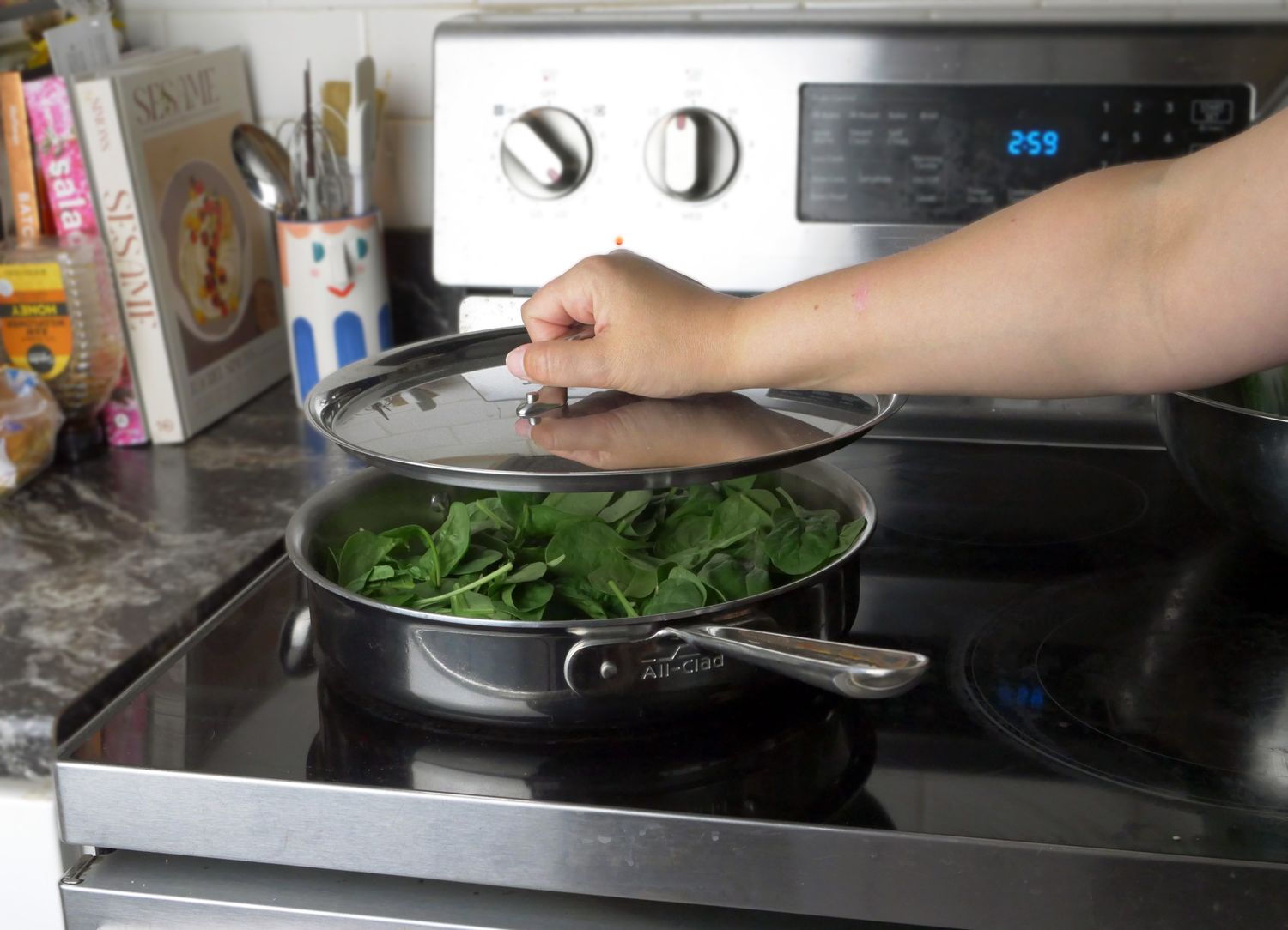 a person putting a lid on a saute pan with spinach
