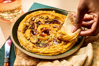 A bowl of sweet potato pepita dip with a person dipping a piece of flatbread