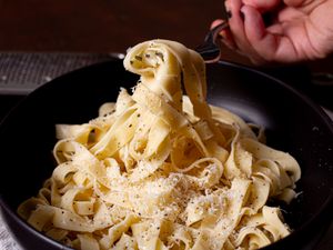 A plate of pasta being twirled on a fork topped with grated cheese and seasoning