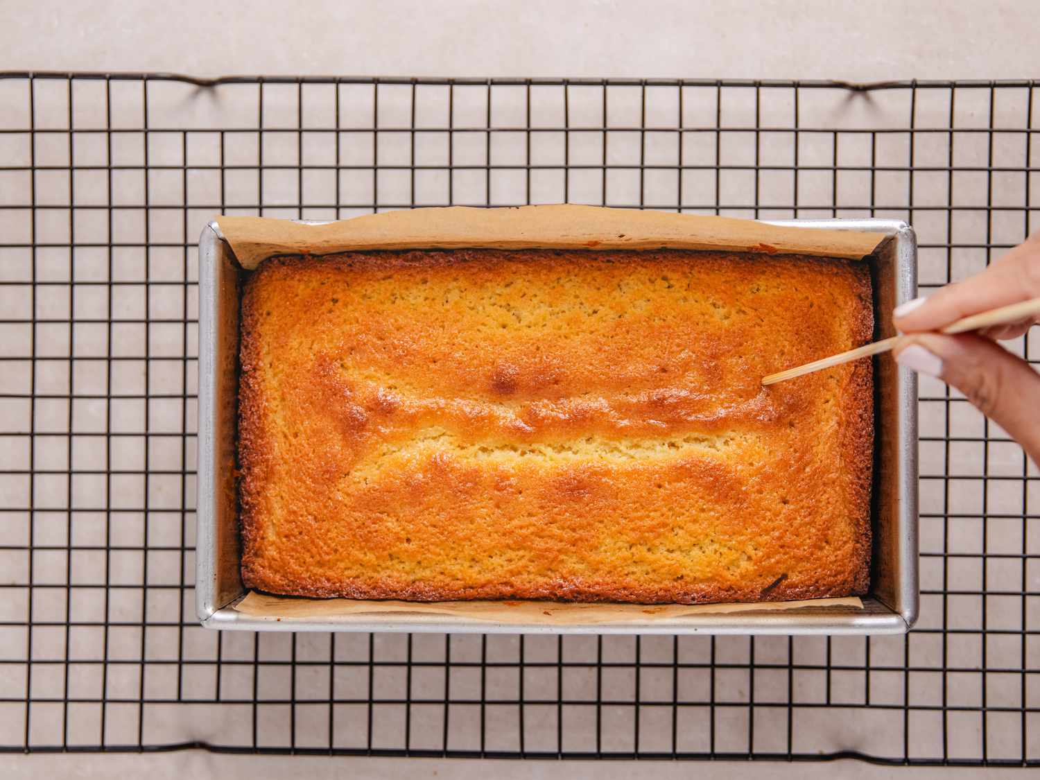 pricking baked cake with skewer in cake tin on a cooling rack