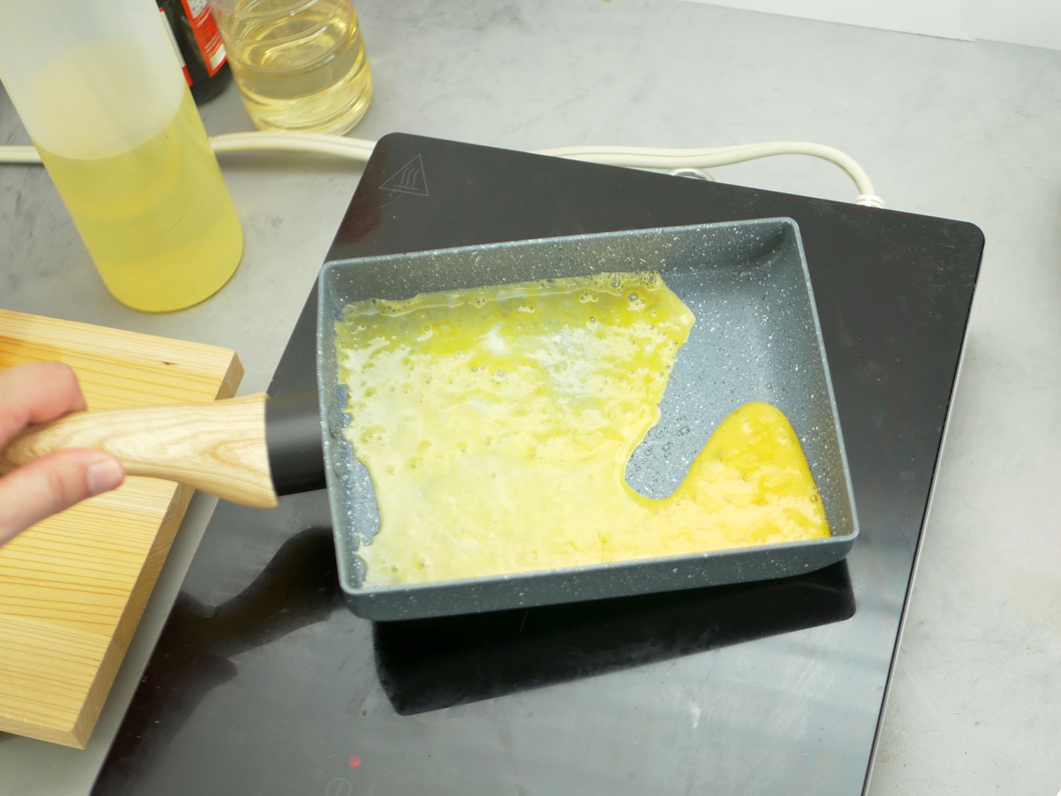 a person tilting the handle on a tamagoyaki pan to swirl the egg around the pan