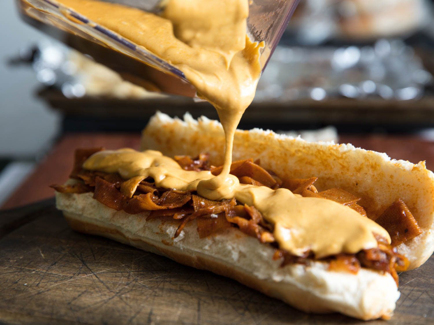 Vegan nacho cheese sauce being poured onto the filling of the vegan philly cheesesteak.