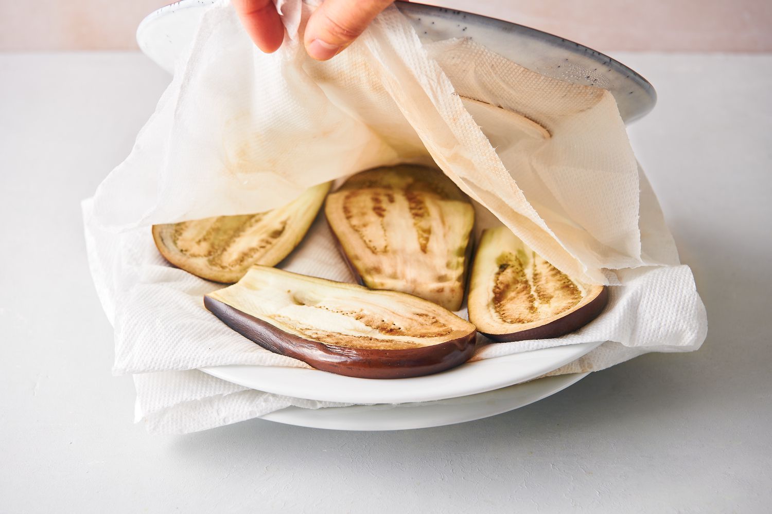 Layers of eggplant slices, paper towels, and plates on a large plate