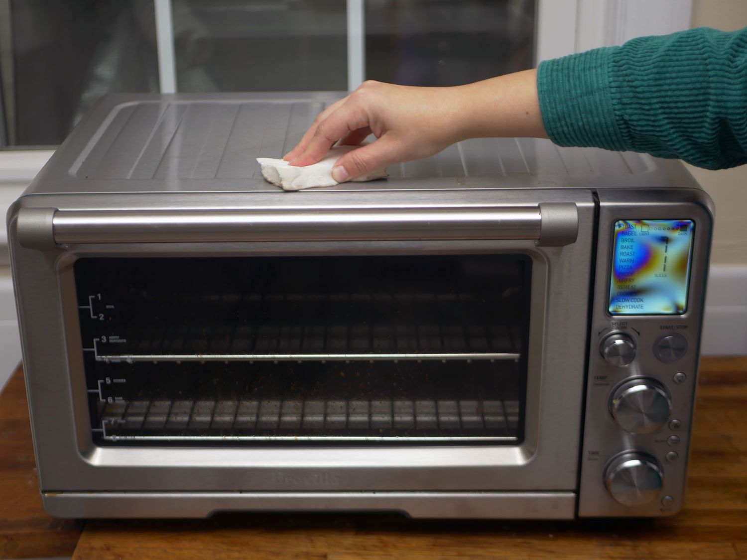 A person using a piece of Magic Eraser to wipe down the exterior of a toaster oven.