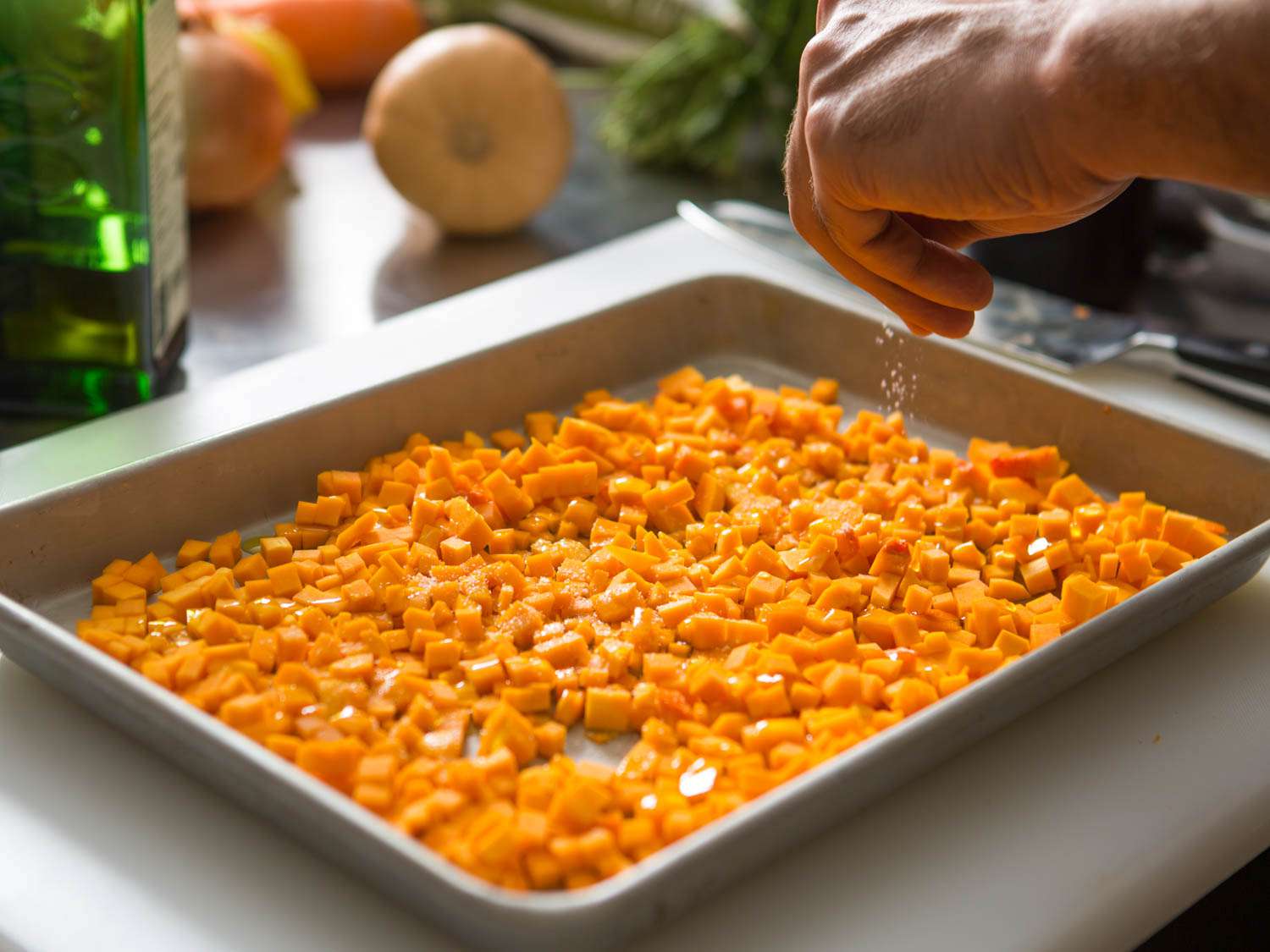 Small-diced squash on a rimmed baking sheet, a hand sprinkling it with salt.