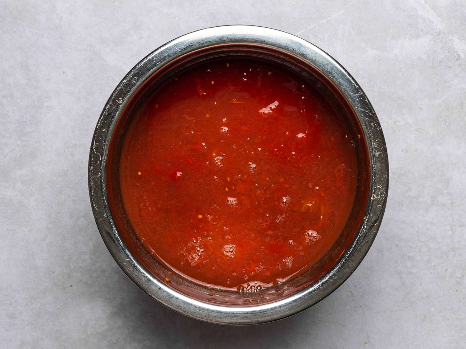A small stainless steel bowl holding chopped tomatoes, chickpea liquid, and juices.