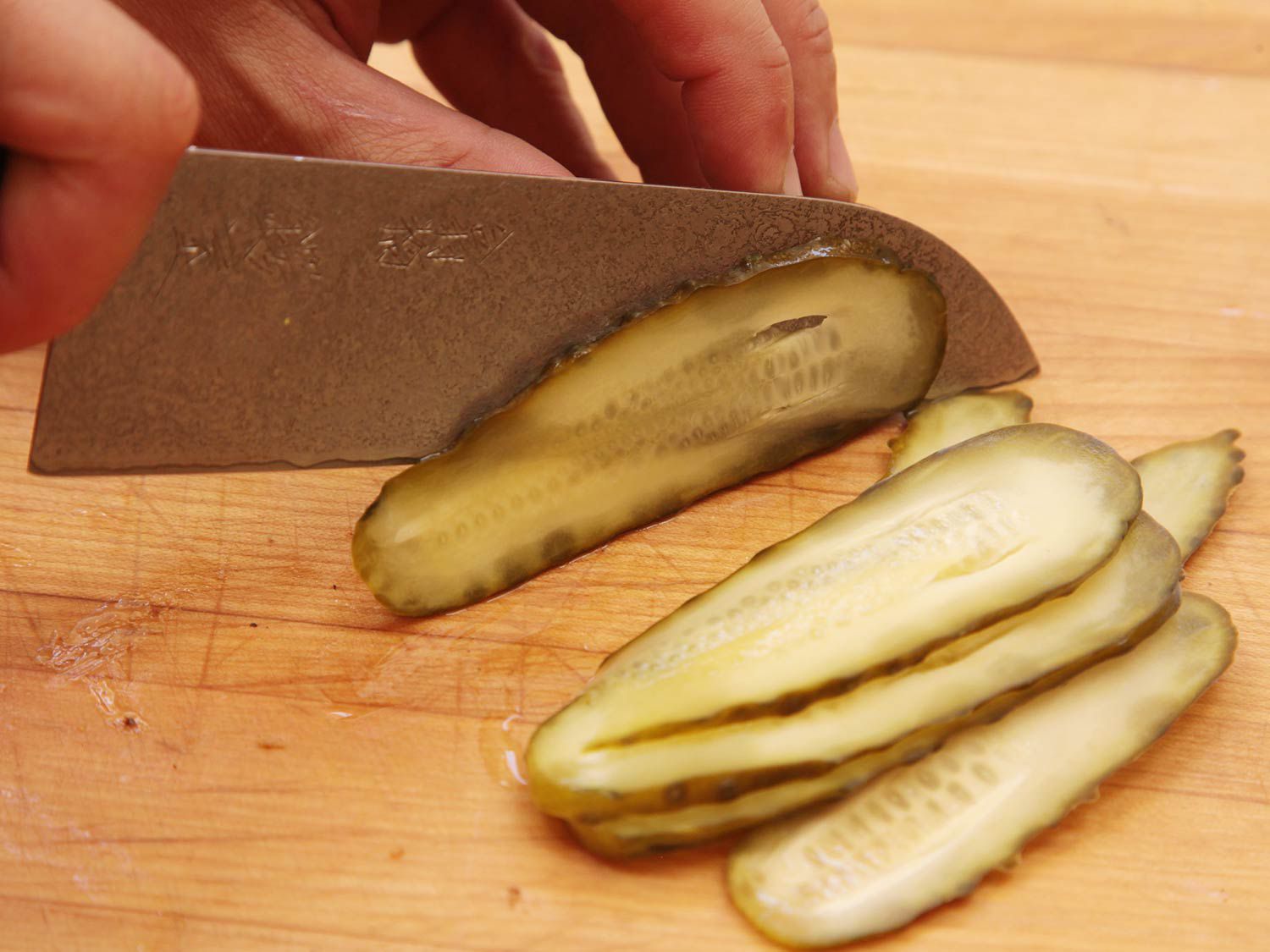 A pickle being sliced along its length with a chef's knife. 