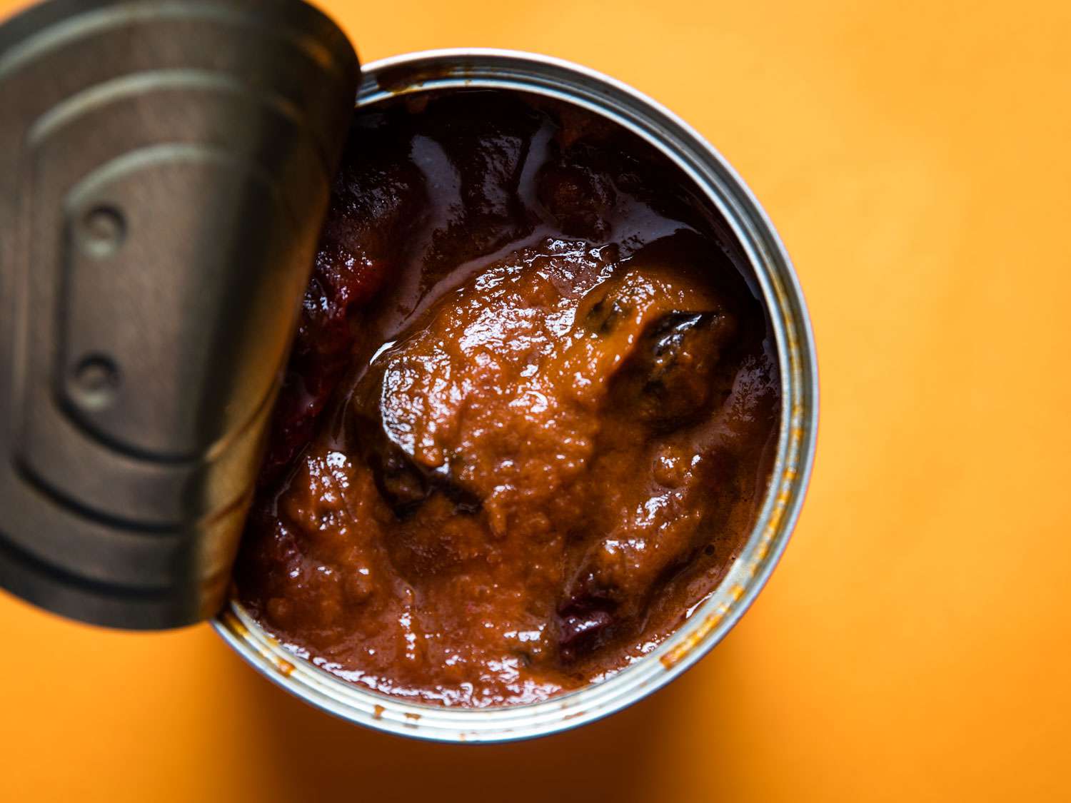 Overhead shot of canned chipotle chilies in adobo sauce, with the lid peeled half off