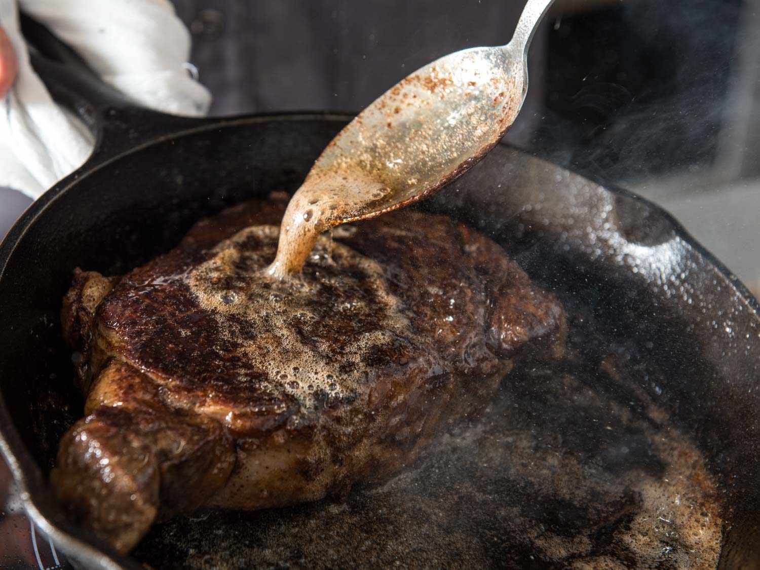 A sauce spoon pouring melted butter over a steak in a cast iron pan