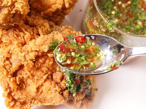 A spoonful of chile-lime-cilantro sauce being drizzled over a piece of fried chicken on a plate. 