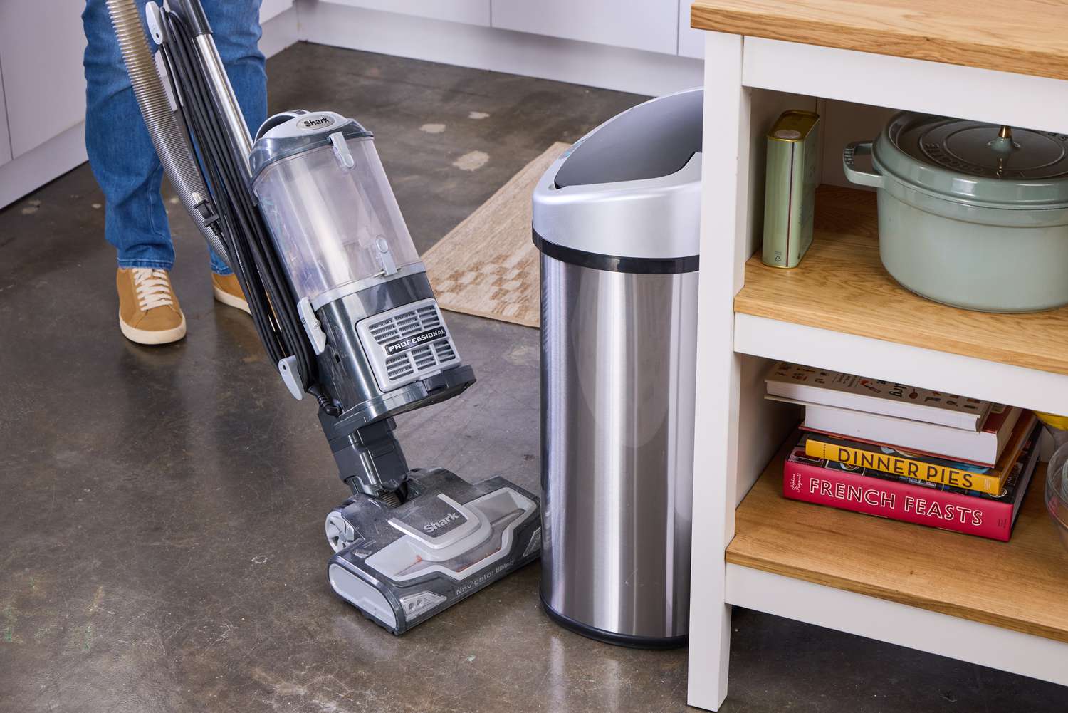 A person vacuums around the iTouchless 13-Gallon Oval Stainless Steel Sensor Trash Can