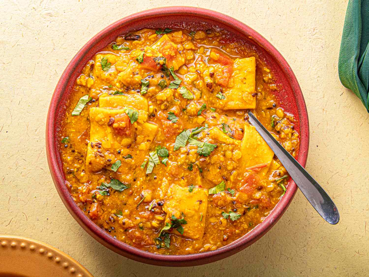 A bowl of dal dhokli with lentils and flatbread pieces garnished with herbs and served with a spoon