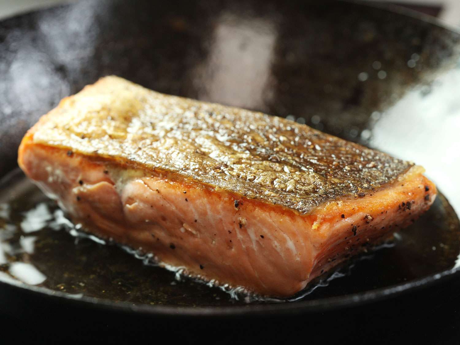 A fillet of skin-on salmon searing in a skillet.