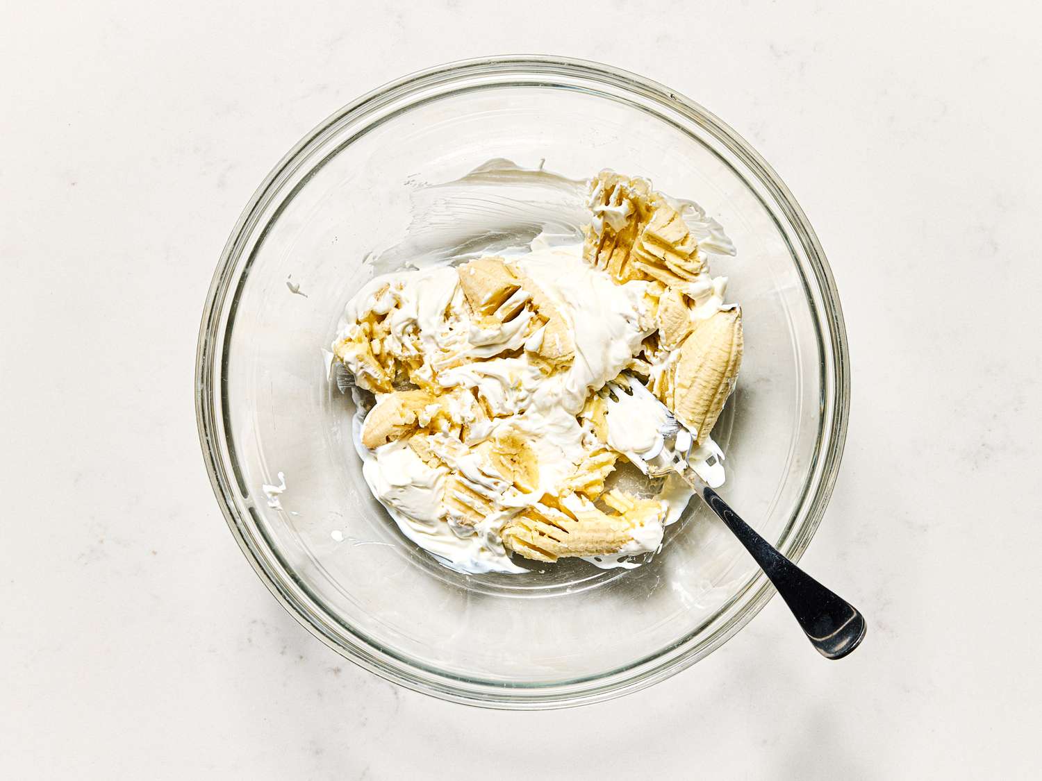 Overhead view of mashing bananas and sour cream