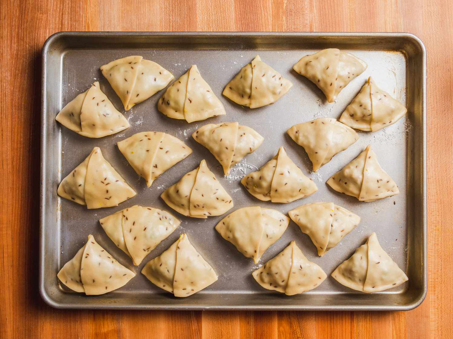 Wrapped samosas on a lightly floured baking sheet, ready for frying.