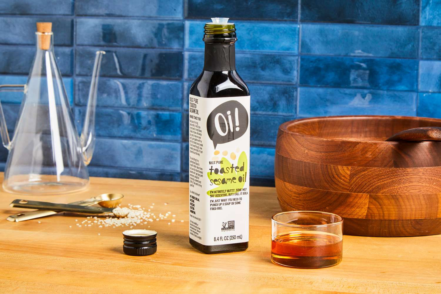 A bottle of toasted sesame oil on a kitchen counter with a wooden bowl and oil pourer