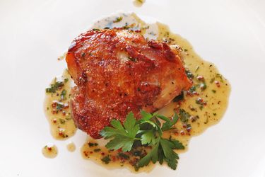 A Crispy Sous-Vide Chicken Thigh on a plate with a pan sauce. 