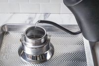 Pouring water into a metallic container using a gooseneck kettle placed on a patterned tray