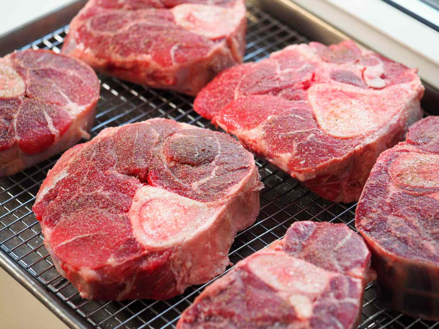 Raw beef shank steaks laid out on a wire rack over a rimmed baking sheet.