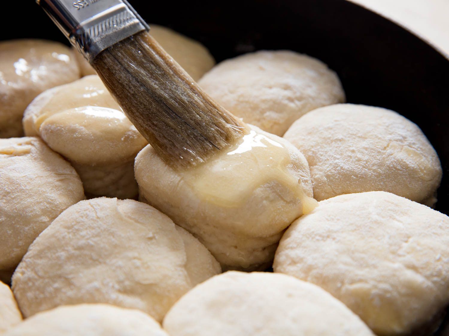 Brushing the risen angel biscuits with butter before baking.