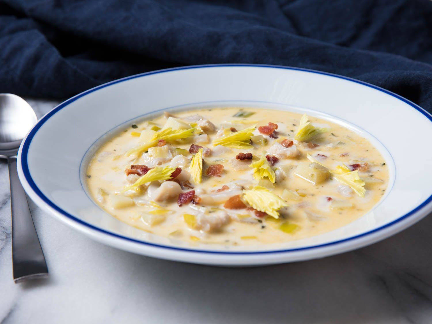 Dish of clam chowder with bacon, garnished with celery leaves.