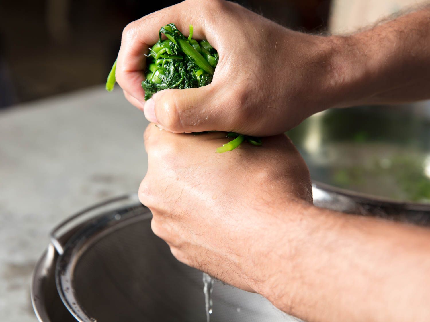 Hands wringing out excess water from blanched spinach.