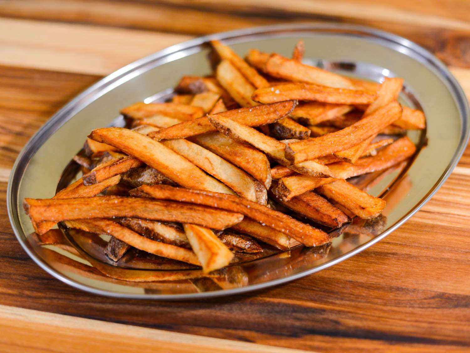 Salted golden crispy fries on a silver plate.