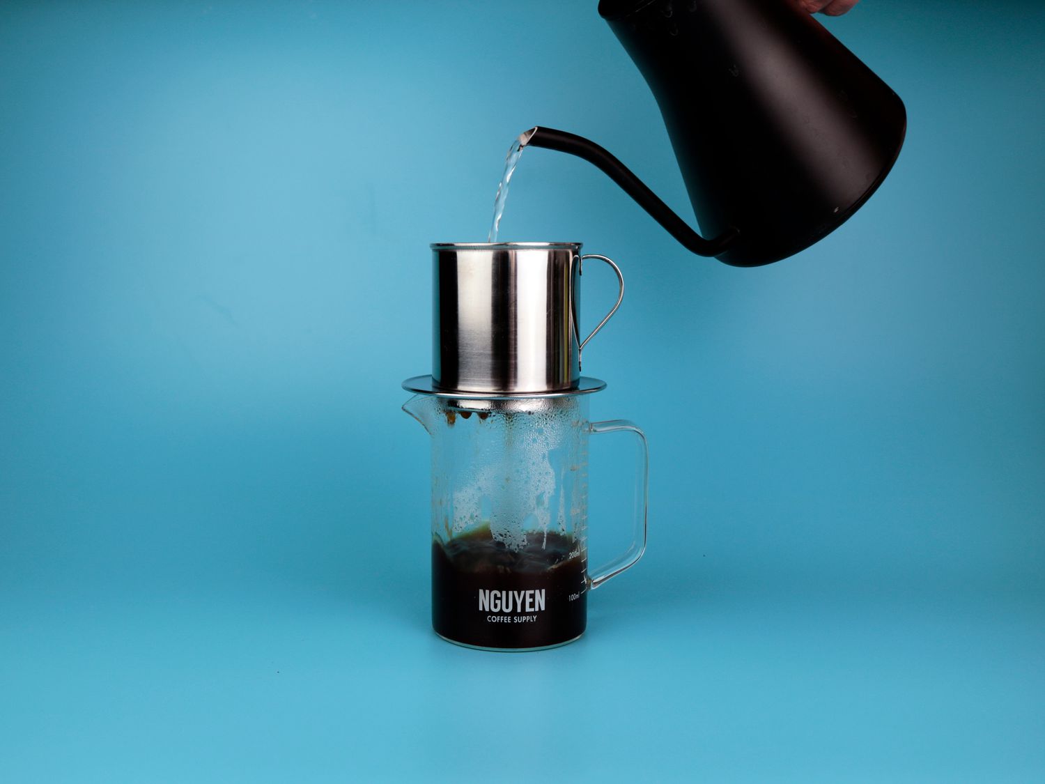 pouring hot water through a phin filter with coffee in the bottom of a large glass mug