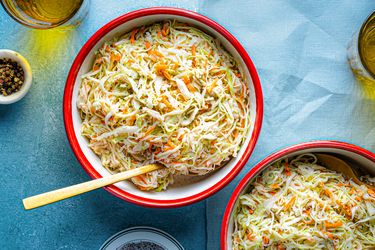 Two bowls of coleslaw with a wooden spoon on one