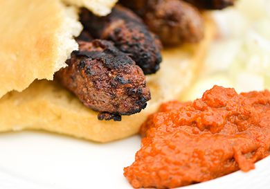 Close-up of cevapi tucked inside Serbian bread with roasted red pepper and eggplant sauce on the side