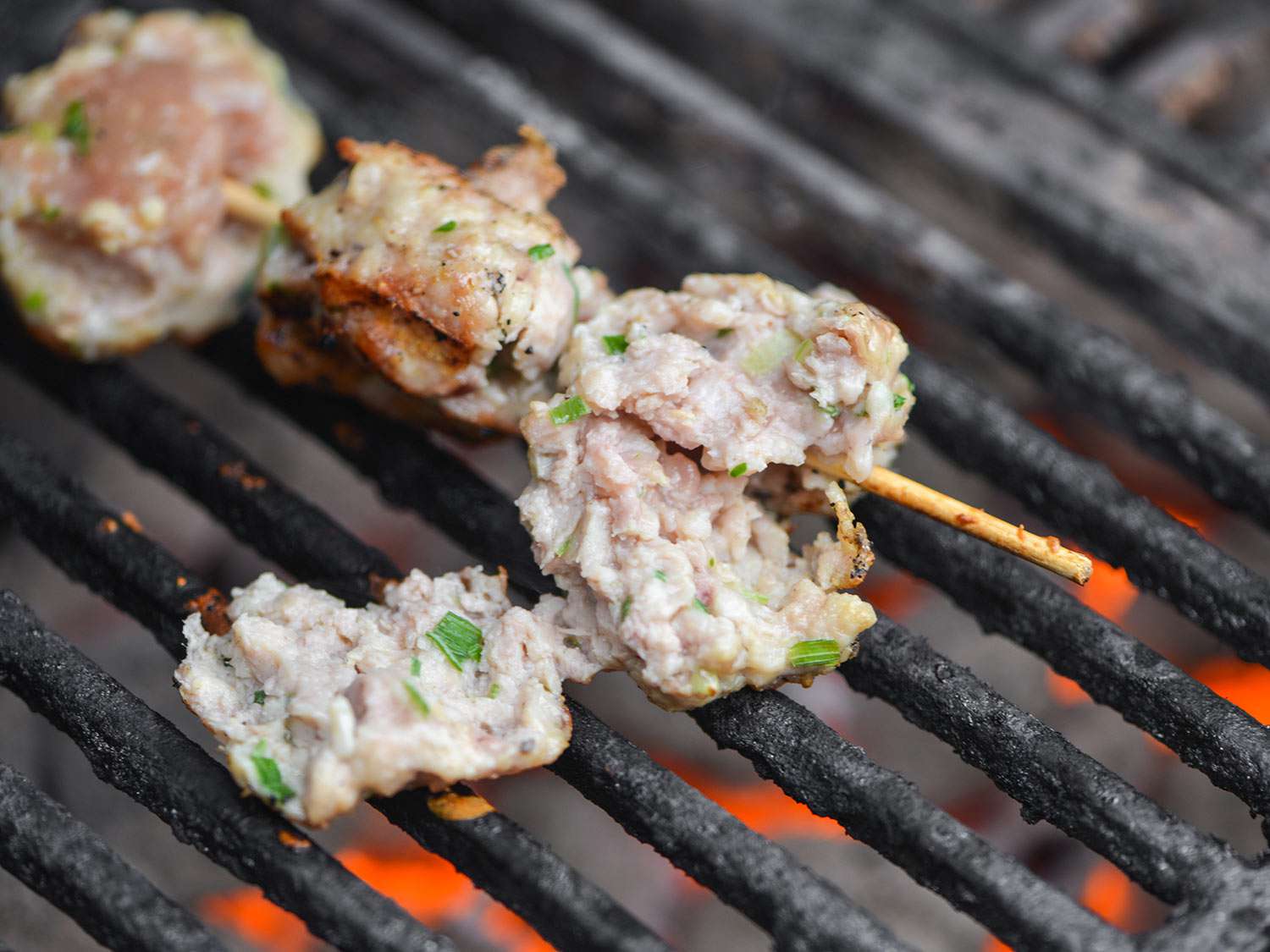A skewer of tsukune meatballs break apart on the grill.