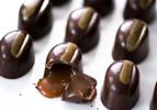 A tray of beautiful chocolate bonbons, with one cracked open to reveal a runny caramel filling.